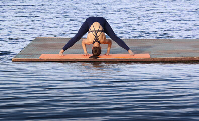 Young latin hispanic woman practicing Prasarita Padottanasana on a sandy beach by the ocean. Morning yoga for flexibility, balance, and inner peace in a serene coastal setting wide legged forward bend