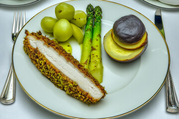 Fine dining dish featuring breaded white fish fillet served with vegetables and potatoes in an elegant setting