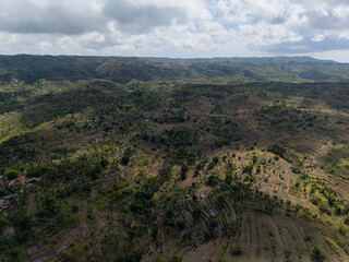 aerial perspective emphasizes varied topography and reforestation efforts beneath cloudy skies Nusa Penida Bali 