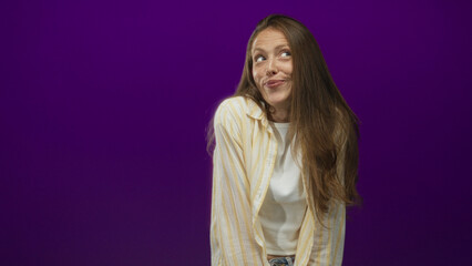 Woman in a striped yellow shirt sticking tongue out toward the camera in a purple studio, leaning forward slightly; playful cheeky attitude.