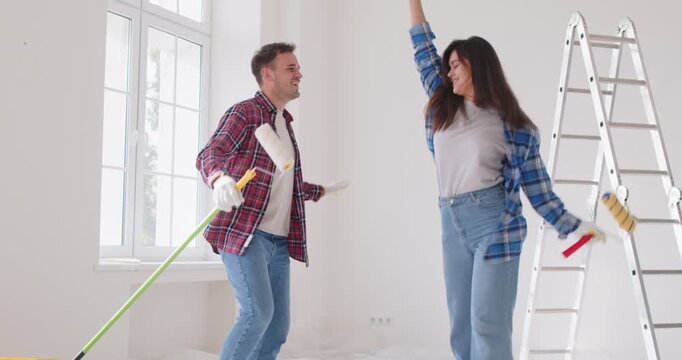 Cheery couple funny dance dreaming planning repair, renovation, dancing after moving into new apartment, happy about interior design home plan, young family enjoys house remodeling, paint color tools 