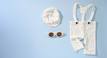 Knitted baby outfit with hat and sunglasses on blue background