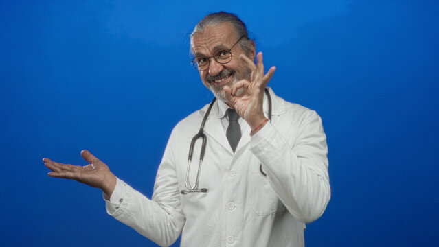 Man doctor points finger to open hand in studio against blue backdrop; health advice wellness confidence.
