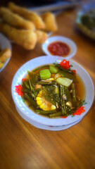 Mixed vegetable tamarind called sayur asem featuring leafy greens, corn, and potato pieces in a rich broth. Cozy, wholesome meal set on a wooden table