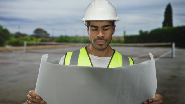 Man holds large blueprint on tenniscourt for ongoing renovation plan; strategic planning determination.