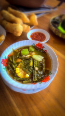 Mixed vegetable tamarind called sayur asem featuring leafy greens, corn, and potato pieces in a rich broth. Cozy, wholesome meal set on a wooden table