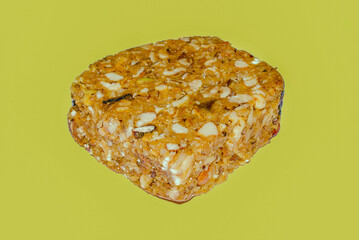 A traditional Indian Karadantu sweet, packed with nuts and jaggery, captured in a close-up shot against a vibrant yellow-green background, highlighting its rich texture.