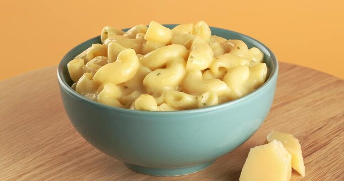 Mac and cheese in a bowl, close-up footage on a rotating table. Parmesan cheese pieces in the background.