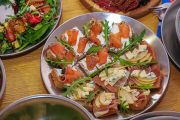 Olivier salad, sandwiches, canapés, bruschetta. A Christmas scene with meat delicacies against a dark wood background. An assortment of cheese and meat appetizers.