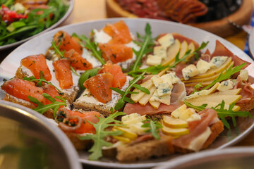Olivier salad, sandwiches, canapés, bruschetta. A Christmas scene with meat delicacies against a dark wood background. An assortment of cheese and meat appetizers.