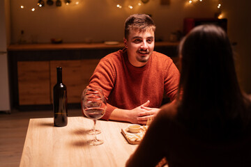 Young man and woman enjoying a romantic, drinking wine on dinner with festive lights, celebrating Valentine's Day. love