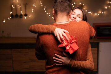 man congratulating happy woman on holiday with red present box, girl hugging boyfriend at home. Happy couple in love. Valentines day