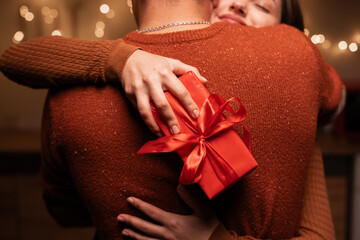 couple celebrating Valentines Day at home. Woman holding red gift box while hugging his lover man