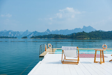 wooden beach chair and coffee table on white raft and swimming pool at waterfront of the open water in natural lake