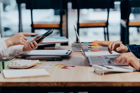 Teamwork in Modern Office: Two professionals collaborate over a shared workspace, one focused on a digital device, while the other navigates a laptop.