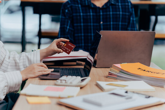 Financial Transaction in progress: Close-up of a business interaction. A person is holding a credit card as another individual uses a laptop, symbolizing a modern and efficient payment.