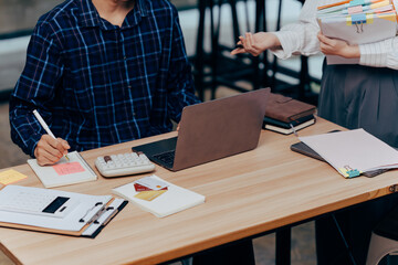 Collaborative Workspace: A dynamic duo collaborates over business endeavors, with a laptop, documents, and calculations creating a vibrant setting of teamwork and ingenuity.