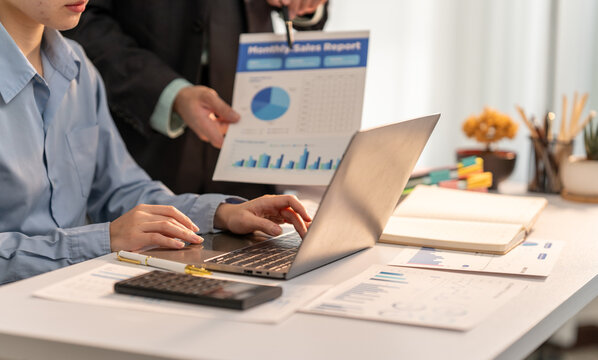 Business Collaboration: A focused professional meticulously analyzes data on a laptop, alongside a colleague presenting sales analytics, illustrating teamwork in a modern workspace.  - Powered by Adobe