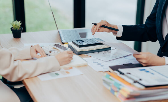 Workplace Collaboration: Two professionals engaged in a focused business meeting. They are seen engrossed in reviewing financial data, working diligently to achieve a successful outcome.