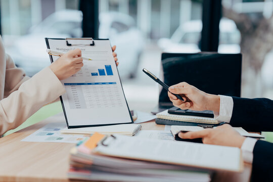 Business meeting: Two individuals engrossed in a focused business meeting, their hands gesture over documents displaying statistical data - Powered by Adobe