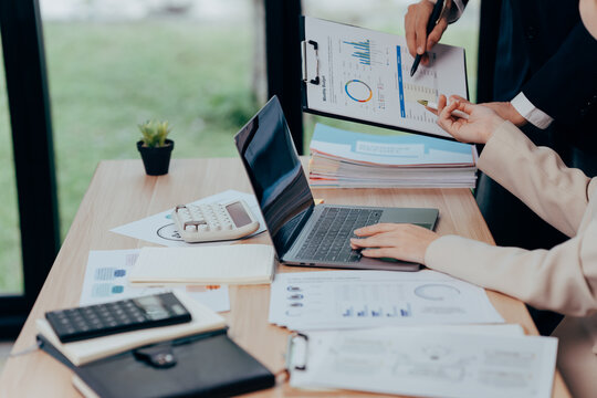 Business analytics teamwork: In a collaborative office setting, colleagues intently analyze financial data on paper documents and laptop, highlighting the strategic focus on numbers.