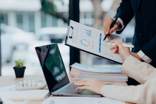 Focused Business Discussion: Two individuals in professional attire engage in a collaborative review of financial data, their attention centered on a detailed report. - Powered by Adobe