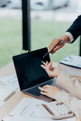 Digital Dialogue: Two figures in a business setting, engaged in focused discussion, collaborate over a laptop, analyzing data and strategizing, illustrating teamwork and professional communication.