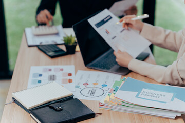 Business Colleagues Analyzing Documents: Close-up of hands examining paperwork during a collaborative business meeting, surrounded by a laptop, notebooks, and business proposal.