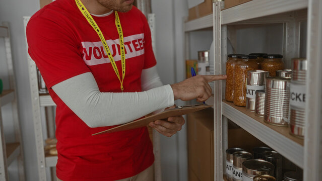 Male volunteer writing on clipboard in charity room surrounded by donation items highlighting his role in an indoor community service setting.