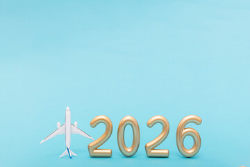 Airplane model and golden 2026 numbers on blue background. Symbol of travel plans and future holiday inspiration. Copy space