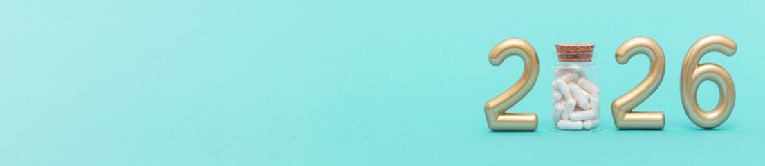 Golden numbers 2026 with a glass jar of capsules on a green background. Symbol of healthcare progress, medical innovation, and future pharmaceutical development. Web banner, copy space
