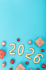 Golden numbers 2026 with festive baubles and gift boxes on blue background. Symbol of new year or Christmas celebration, holiday mood and winter happiness. Copy space, vertical photo
