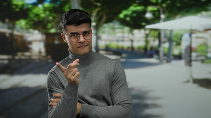 Young man in glasses pointing to himself with a playful expression on a sunny city street,...