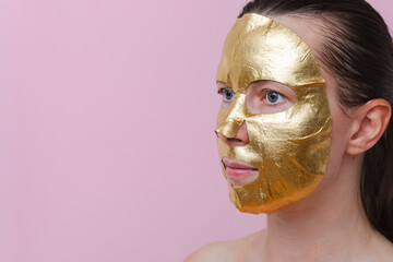 A woman with a golden facial mask against a pink background. The image represents self‑care, beauty and personal wellness. Copy space