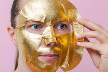 A woman removes a golden sheet mask from her face. The picture conveys beauty, renewal, confidence, and self‑care.