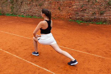 Woman stretching legs on clay tennis court. Concept of sports training, flexibility, preparation and physical wellness through outdoor athletic activity.