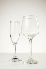 Two empty glassware pieces—a champagne flute and a wine glass—stand side by side on a white...