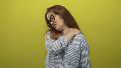Woman wearing glasses and a striped shirt clutching her right shoulder in a bright green studio set; discomfort.
