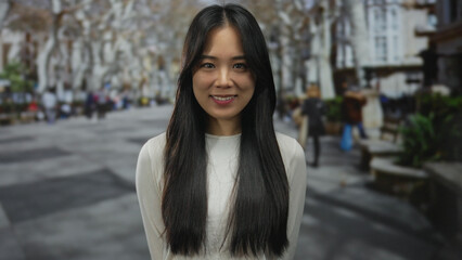 Fototapeta premium Young chinese woman smiling on a bustling street outdoors with natural light highlighting the lively atmosphere.