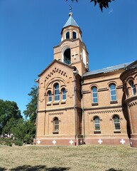 Majestic red brick church with ornate bell tower standing against a vibrant blue sky