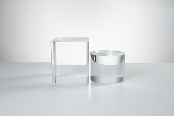 Clear acrylic cube and cylinder displayed on white surface with soft lighting and minimal design.