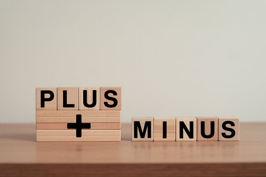 Wooden blocks spelling plus and minus on a wooden surface showcasing mathematical concepts and financial comparisons with a focus on addition subtraction and balance in a neutral setting