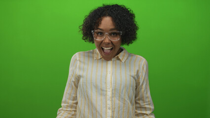 Obraz premium Woman with curly hair wearing glasses and a striped shirt smiles in a green studio portrait; joyful optimism.