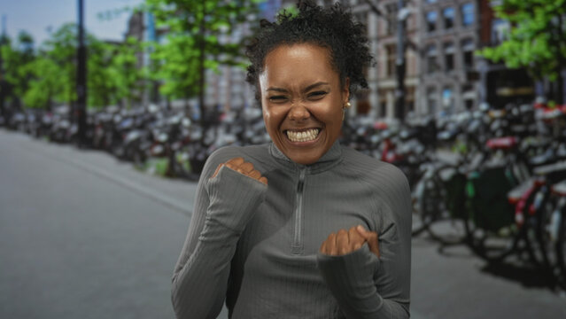 Young african american woman counts fingers with broad smile on busy street lined with bicycles; victory joy.