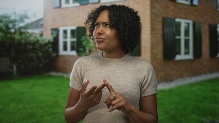 Young african american woman pointing finger at palm at brick home entrance outdoors; confusion...
