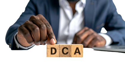 A person in a suit arranges wooden blocks spelling "DCA." Partially visible laptop