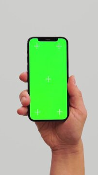 Male hand using chroma key smartphone on White background. Blank green screen mock up with Tracking Markers. Hand lifts phone up