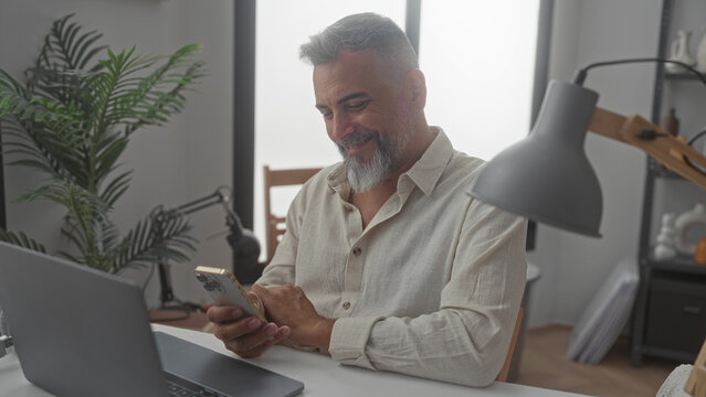 Man holding smartphone at a desk in an office, tapping the screen while seated and smiling; calm productivity.