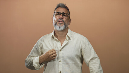 Fototapeta premium Man middle aged gesturing with hands and adjusting shirt collar in studio with peach backdrop; frustration self reflection.