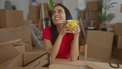 Woman smiling while holding a yellow cup surrounded by cardboard boxes in a cozy new apartment filled with unpacked items suggesting a fresh start.